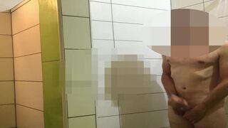 A men wanks in public shower while people wait for showering