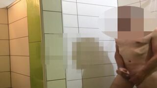 A men wanks in public shower while people wait for showering